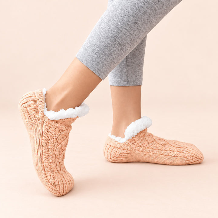 Apricotfarbene Thermosocken in seitlicher Trageansicht, ein Fuß flach und einer auf der Zehenspitze, vor hellem pfirsichfarbenem Hintergrund.