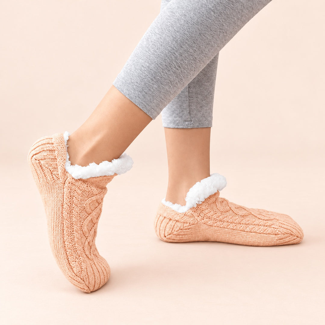 Apricotfarbene Thermosocken in seitlicher Trageansicht, ein Fuß flach und einer auf der Zehenspitze, vor hellem pfirsichfarbenem Hintergrund.