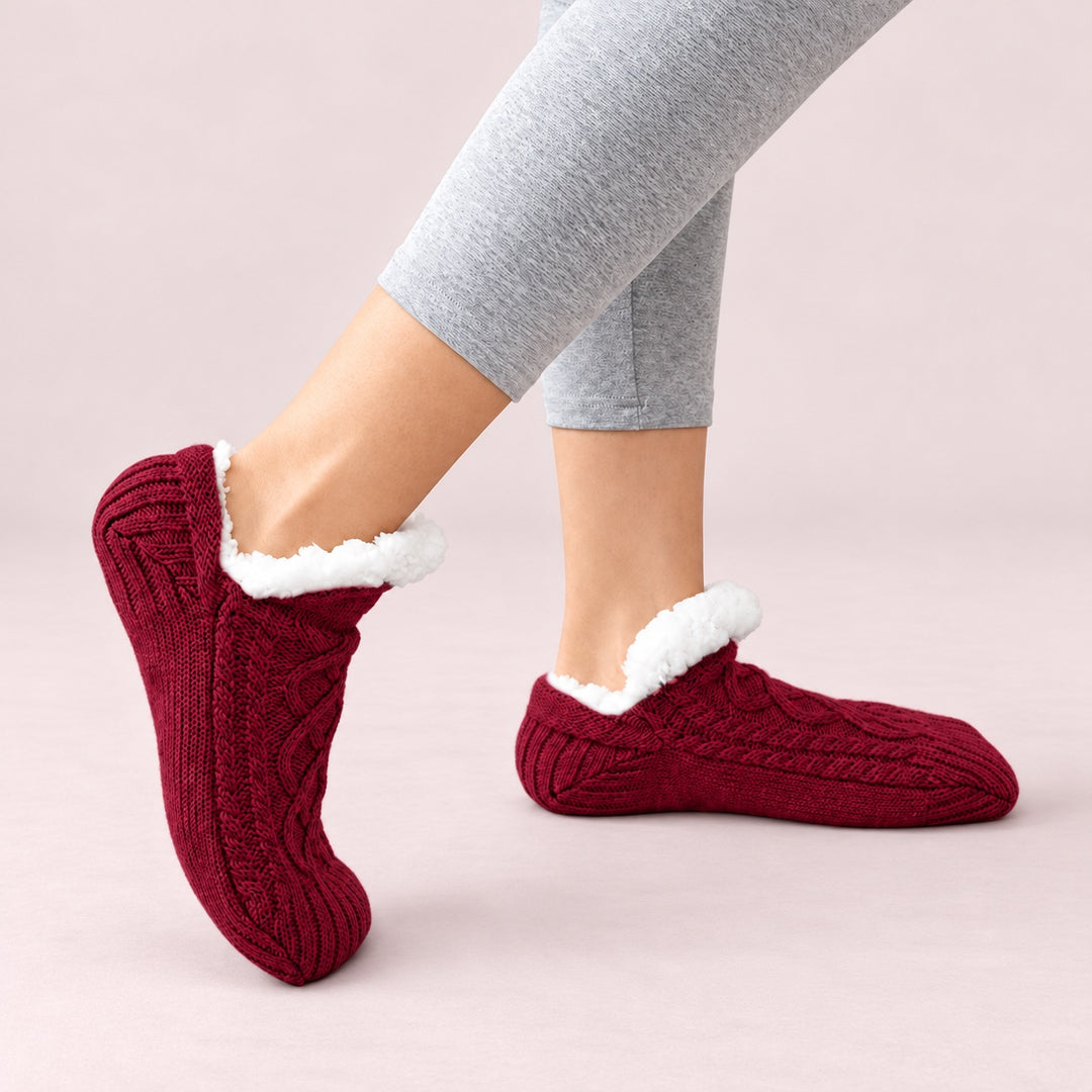 Bordeauxrote Thermosocken in seitlicher Trageansicht, ein Fuß flach und einer auf der Zehenspitze, vor zartrosa Hintergrund.