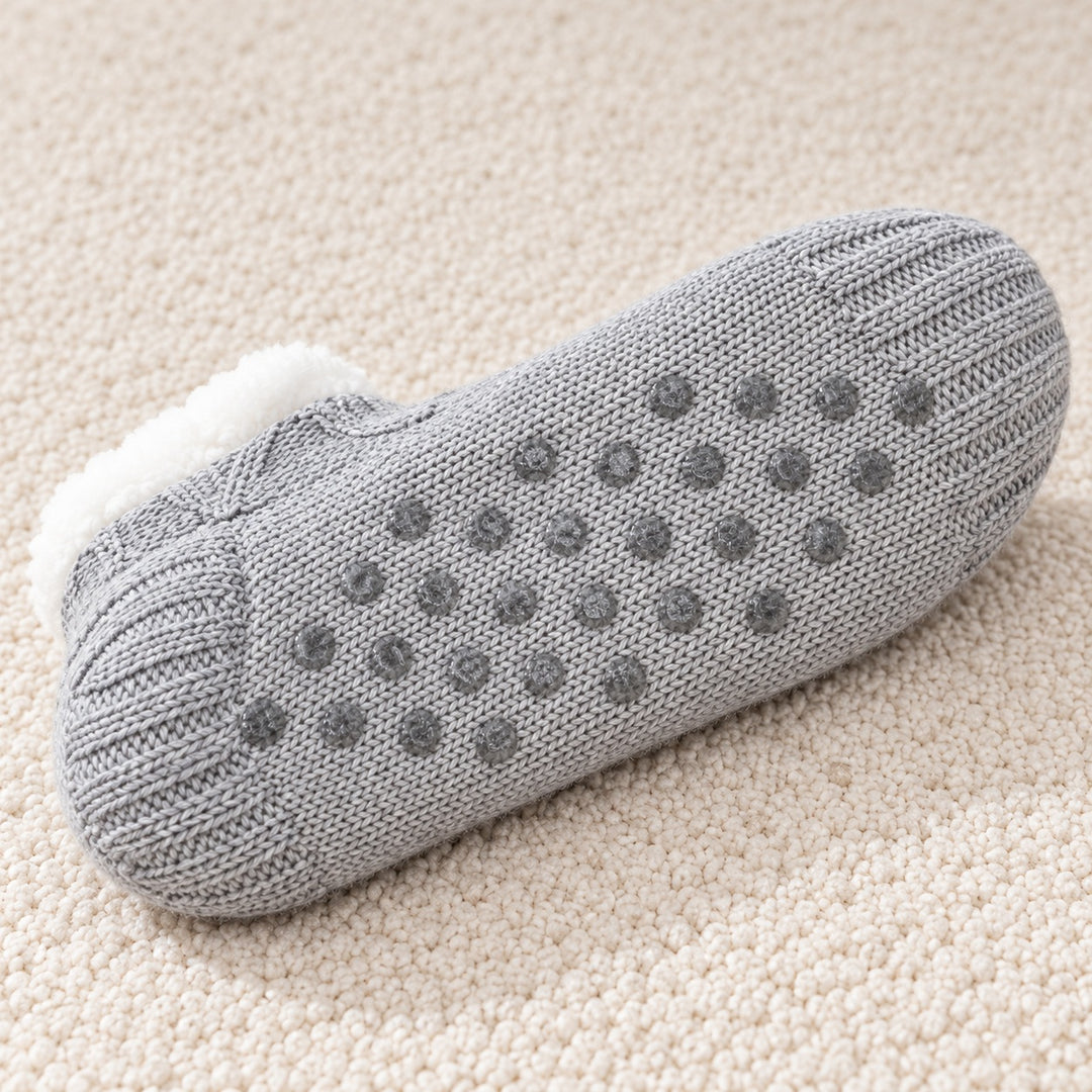 Nahaufnahme der grauen Textilsohle mit Antirutschnoppen auf einem cremefarbenen Teppich.