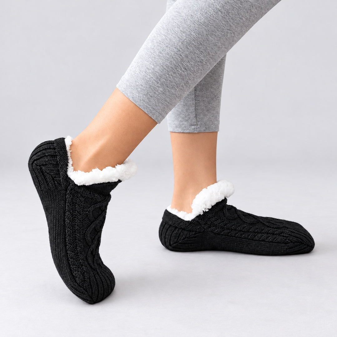 Schwarze Thermosocken in seitlicher Trageansicht, ein Fuß flach und einer auf der Zehenspitze, vor hellgrauem Hintergrund.