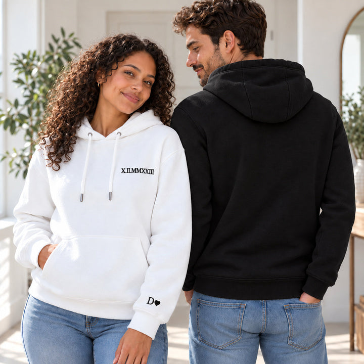 Femme de face en sweat blanc brodé en noir et homme de dos en sweat noir uni, capuches et coupe des pulls couple visibles.