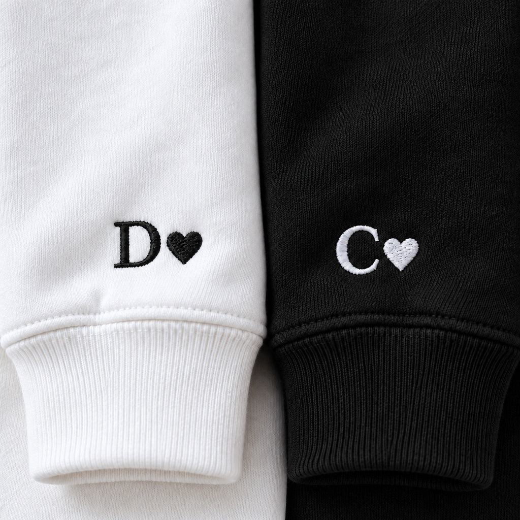 Gros plan des poignets : initiale D et cœur noirs sur le sweat blanc, initiale C et cœur blancs sur le sweat noir.