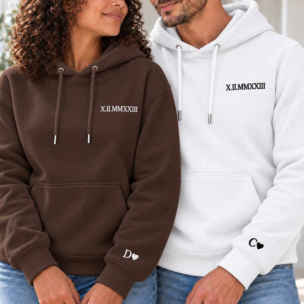 Couple en sweats personnalisés : femme à gauche en marron et homme en blanc, date en chiffres romains à la poitrine et initiales avec cœurs aux poignets.