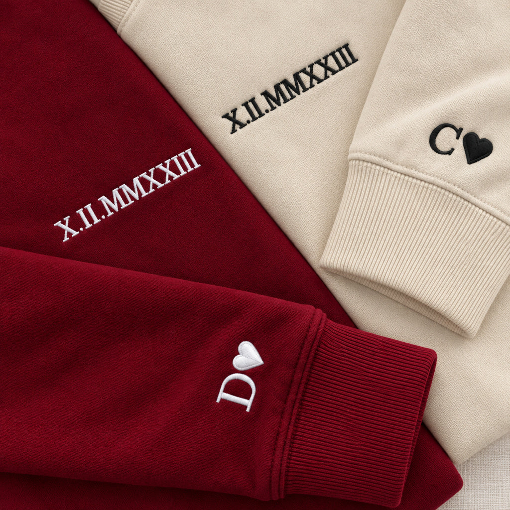 Détail des dates brodées et des poignets : D et cœur blancs sur le sweat bordeaux, C et cœur noirs sur le sweat beige.