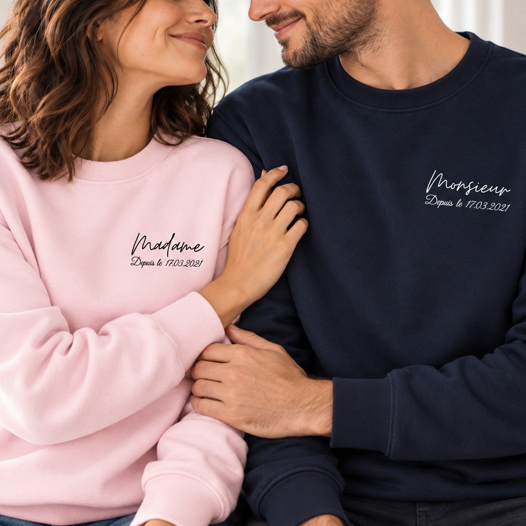 Vue rapprochée d’un couple en sweats Madame rose et Monsieur bleu marine, montrant les inscriptions et la date personnalisée.