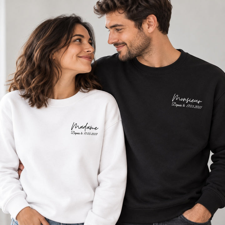 Couple portant les sweats personnalisés Madame blanc et Monsieur noir, avec leur date imprimée sur la poitrine.