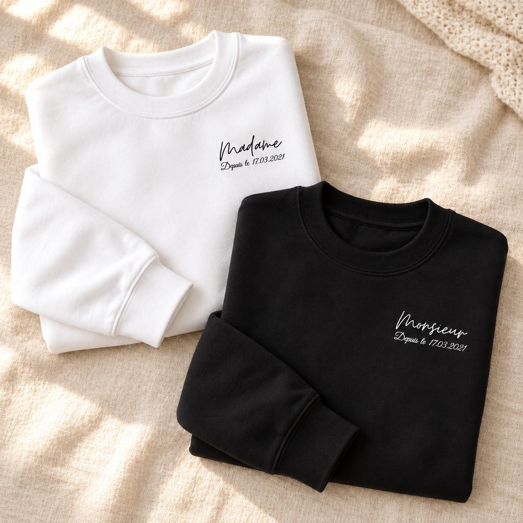 Sweats Monsieur et Madame personnalisés pliés, noir et blanc, avec date imprimée sur la poitrine, sur un fond de lin clair.