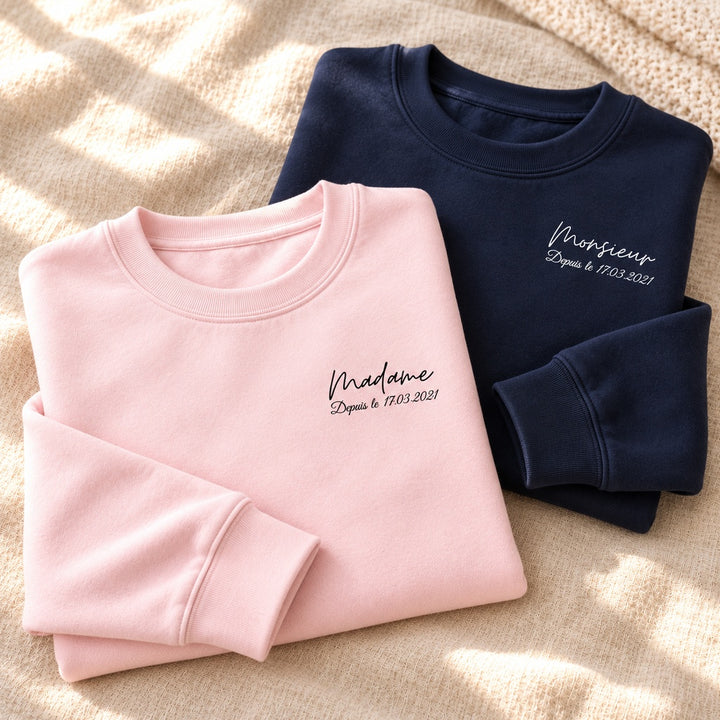 Duo de sweats personnalisés pliés, Madame rose et Monsieur bleu marine, avec date imprimée et fond lumineux en lin.