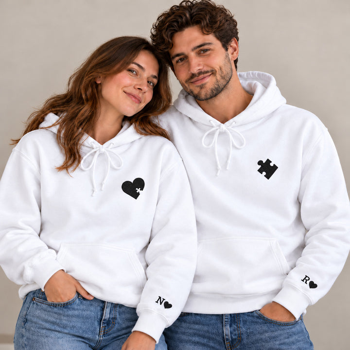Couple en sweats blancs personnalisés avec cœur et pièce de puzzle brodés noirs, initiales N et R aux poignets.