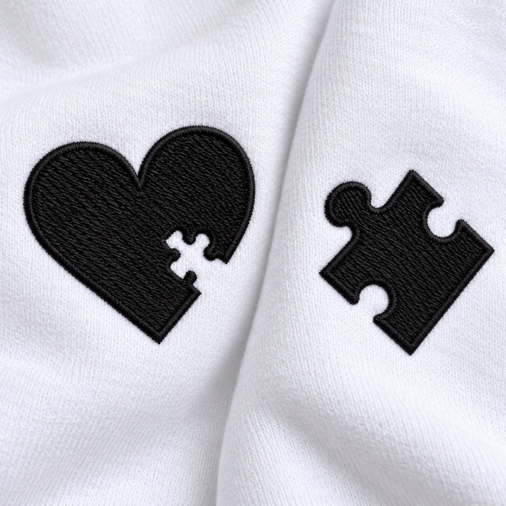 Macro du cœur à découpe puzzle et de la pièce de puzzle brodés en fil noir sur le tissu blanc des sweats couple.