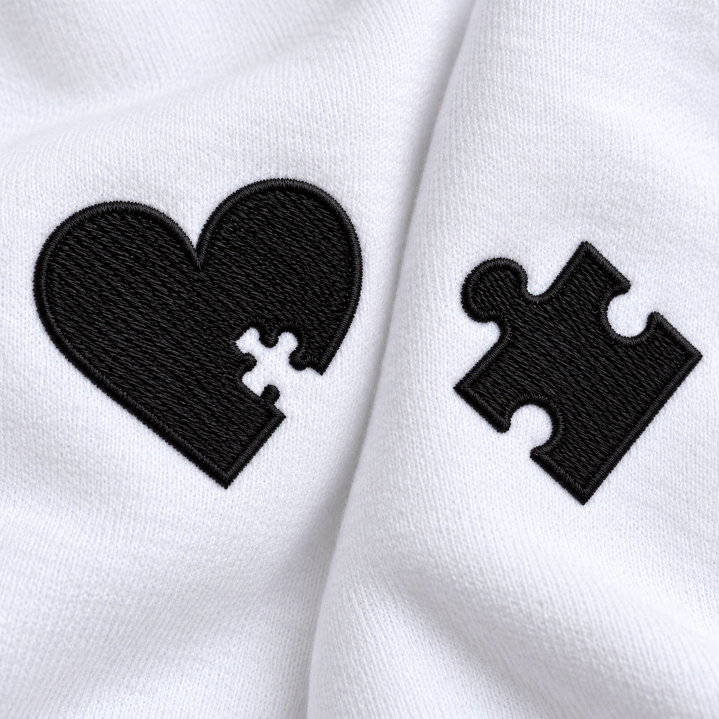 Macro du cœur à découpe puzzle et de la pièce de puzzle brodés en fil noir sur le tissu blanc des sweats couple.