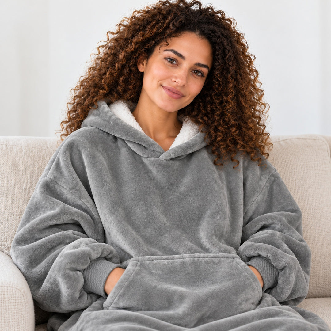 Femme portant le sweat plaid gris, assise sur un canapé beige, cadrée du visage à la taille.