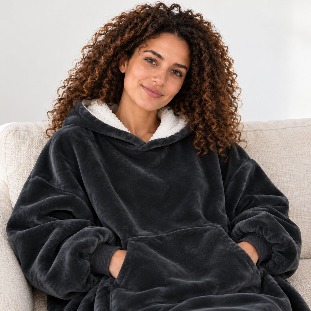 Femme portant le sweat plaid noir, assise sur un canapé beige, cadrée du visage à la taille.