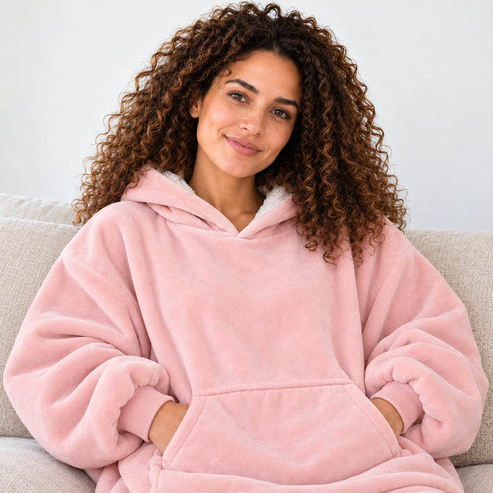 Femme portant le sweat plaid rose clair, assise sur un canapé beige, cadrée du visage à la taille.